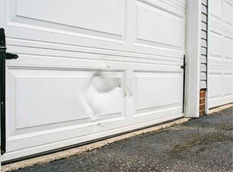 a dented lower steel panel on a white residential garage door in a New Jersey driveway.