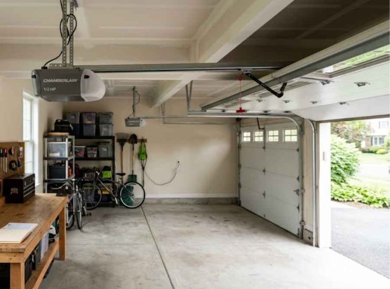 suburban residential garage interior featuring a ceiling-mounted opener, workbench with documentation, and daylight from an open door.