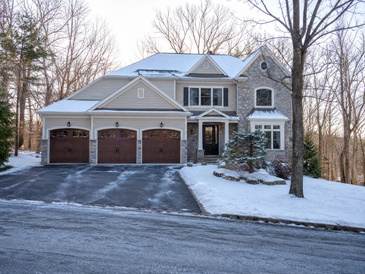 A dark brown wood-grain steel garage door on a stone and siding home with a light dusting of snow and evergreens